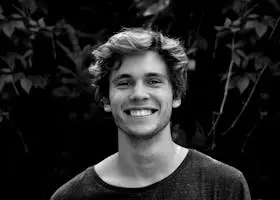 Home A black and white portrait of a young man smiling outdoors with natural background.